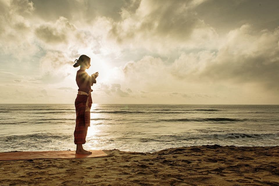 Yoga practitioner in namaste at sunrise on the beach